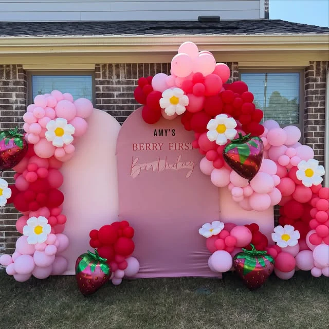 Pink and red strawberry-themed first birthday balloons and event backdrop